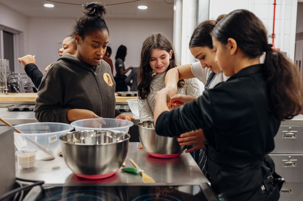 Grŵp o bedwar o bobl ifanc wedi ymgynnull o amgylch powlenni cymysgu yn ystod sesiwn Technoleg Bwyd
