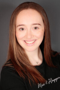 Image of Jasmine Brittan. She has red hair and a black top on that says "make it happen"